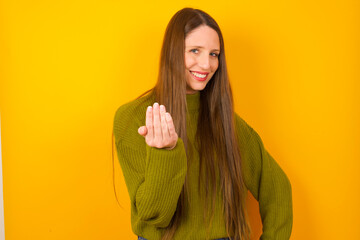 Young beautiful Caucasian woman wearing green sweater against yellow wall inviting to come with...