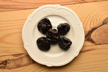 Sweet organic prunes on a plate, close-up, on a wooden table.