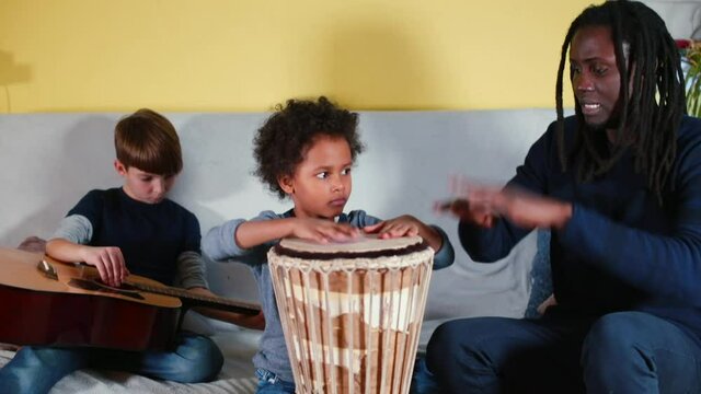 Black father teaches children to play son's drum. Shows the technique of striking jambe with his hands. Transfer of knowledge to the generation. Training of technique and musical ear.