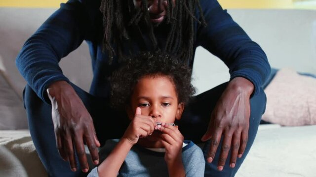 Black child playing harmonica sitting at the feet of a single father, Learning music. A man with dreadlocks sits over a child. Spending time with his family.