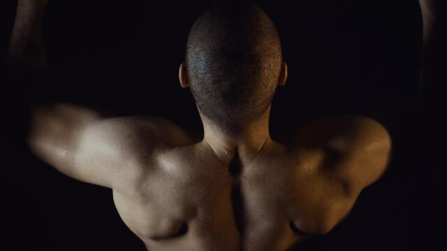 Portrait of a muscular man squeezing in a gym studio. Man doing pull ups. Strong young man training.