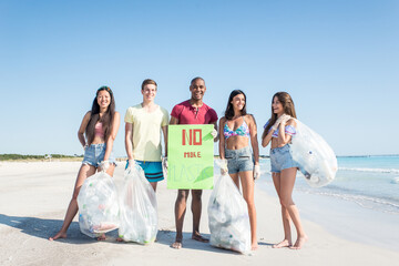 Group of activists friends collecting plastic waste on the beach. People cleaning the beach up,...