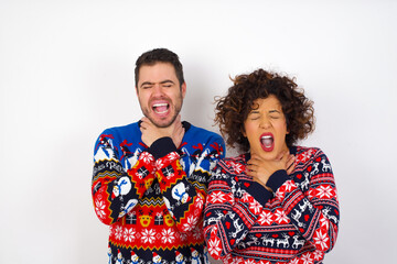 Young couple wearing Christmas sweater standing against white wall shouting suffocate because painful strangle. Health problem. Asphyxiate and suicide concept.