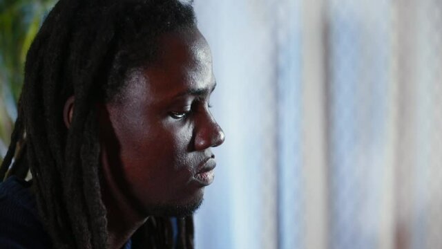 Portrait of a black man with dreadlocks in focus. He turns his head, looks at the camera. Tired look of a man after work.