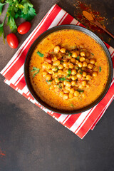 Hot spicy soup with chickpeas, onions, and tomato in a black ceramic bowl on a dark background top view. Tasty vegetarian food, Indian dish. Copy space for text.