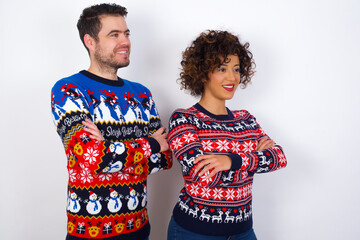 Young couple wearing Christmas sweater standing against white wall cross hands look copy space