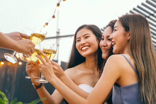 Happy Asian Woman Teenagers Cheering And Toast With White Sparkling Wine Glass To Celebrating At Dinner Party In Summertime. Celebration, Relationship And Friendship Concept.