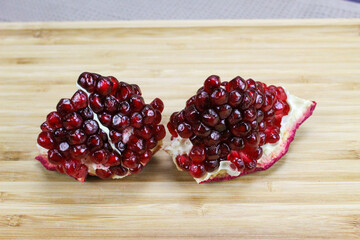 Two pieces of pomegranate with red seeds on a wooden tray. Pomegranate seeds. One piece next to...