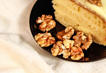 Part of a sponge cake on a black saucer and walnuts next to it.