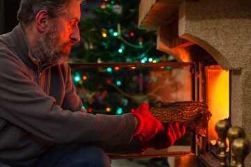 Man sits in front of burning fireplace. Behind Christmas tree