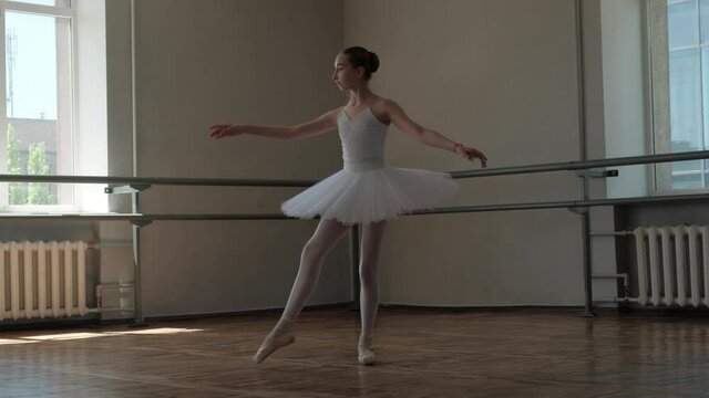 A ballerina in a white tutu trains and dances beautifully.