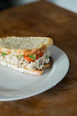 Tuna salad sandwich on toasted white bread with sliced avocado and tomato on white plate