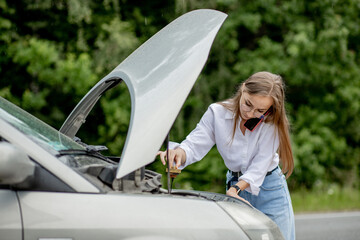 Young woman opening bonnet of broken down car having trouble with her vehicle. Worried woman talking on the phone near broken car. Girl model standing near the broken car calling for auto service
