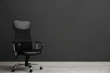 Comfortable office chair near black wall indoors. Space for text