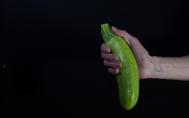Fresh zucchini, on black background in the hand of a Caucasian