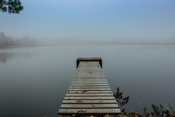 Mysterious morning by lake. Foggy autumn mystery atmosphere. Wooden pier on the pond.Magic mood. Misty fall day. Speechless place. Relaxing meditation without people.Silence scene.Serenity background.