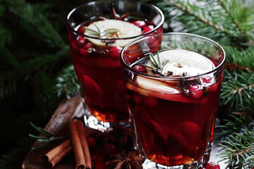 Mulled red wine with cranberry, apple and spices: anise, cinnamon, rosemary and cloves on dark moody black background and fir branches, winter christmas coctail, holiday hot drink, closeup