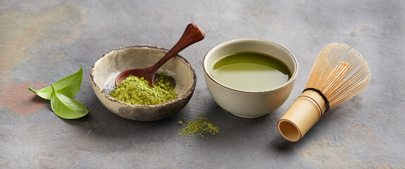 Green matcha powder with chasen bamboo whisk and leaves camellia sinensis on gray background