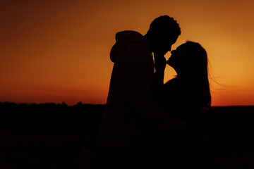 Silhouettes of lovely couple, handsome man gently hug beautiful woman at sunset, enjoy tender moments, caring husband and loving wife spend time together, weekends outdoors concept