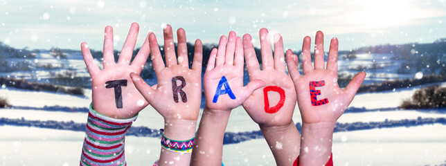 Children Hands Building Colorful English Word Trade. Snowy Winter Background With Snowflakes