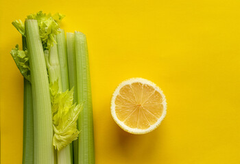 A slice of lemon and a bunch of celery lie on a yellow background