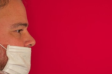 man in profile with white hygienic mask on red background.