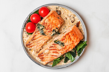 Salmon fillet with creamy sauce, spinach and tomatoes on white background. top view. Healthy food
