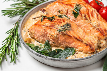 Grilled salmon steak with cream sauce, spinach, tomatoes and rosemary on white marble background. close up