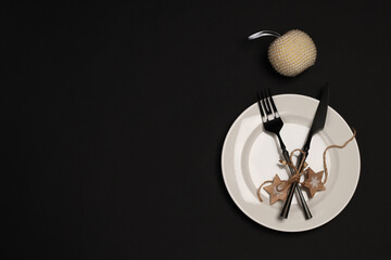 New Year and Christmas table setting. White plate, pearl apple, black cutlery on a black...