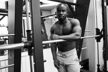Fototapeta na wymiar Black and white portrait of a brutal African American man who stands in the gym. Sexy Muscle Fitness Trainer