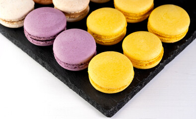 Macarons are laid out on a black slate in beautifully colored rows.