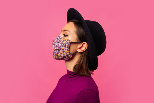 Studio  photo  of young  brunette  girl  wearing respiratory face mask against coronavirus. Background of  pink color with copy space.