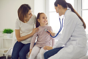 Young smiling woman pediatrician using stethoscope for checking up little smiling girl