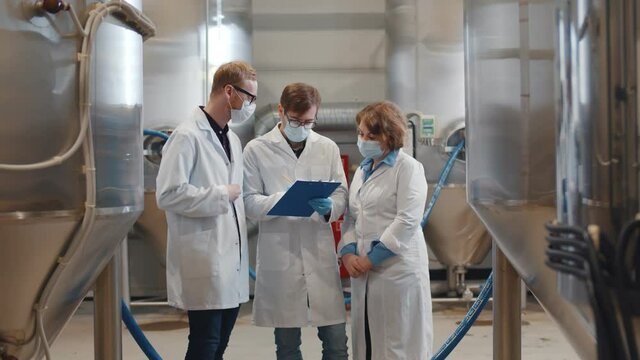 Group of young inspectors in white coat and safety mask conducting audit at beer factory.