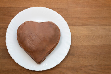 Heart-shaped cake base on a white plate. Wooden background.