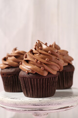 Delicious chocolate cupcakes with cream and beads on white stand, closeup