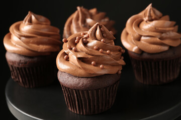 Delicious chocolate cupcakes with cream and beads on black table, closeup