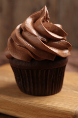 Delicious chocolate cupcake with cream on wooden board, closeup