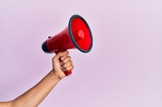 Hand of hispanic man holding megaphone over isolated pink background.