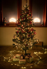 Christmas lights and ornaments on a christmas tree. Candle style christmas lights in the background. Present under the christmas tree.