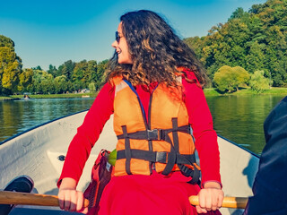 Beautiful long-haired brunette woman in an orange life jacket rowing oars while sitting in a boat....