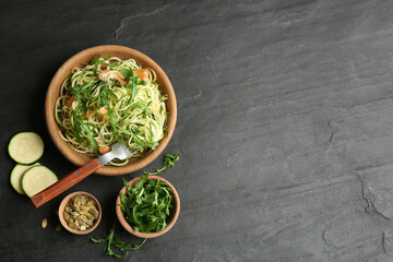 Delicious zucchini pasta with shrimps and arugula served on black slate table, flat lay. Space for...