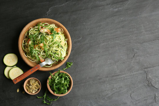 Delicious zucchini pasta with shrimps and arugula served on black slate table, flat lay. Space for text