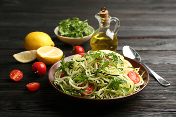 Delicious zucchini pasta with cherry tomatoes and arugula served on black wooden table
