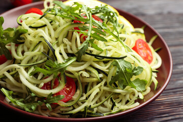 Delicious zucchini pasta with cherry tomatoes and arugula on black wooden table, closeup