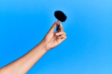 Hand of hispanic man holding makeup brush over isolated blue background.