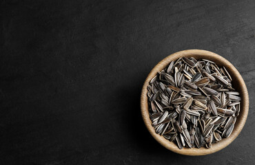 Raw sunflower seeds in bowl on black table, top view. Space for text