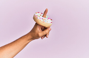 Finger of hispanic man holding donut over isolated pink background.