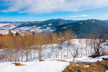 mountainous countryside on a sunny day. late winter scenery or beginning of spring. melting snow and leafless trees on the hills. village in the distant valley. transcarpathia, ukraine