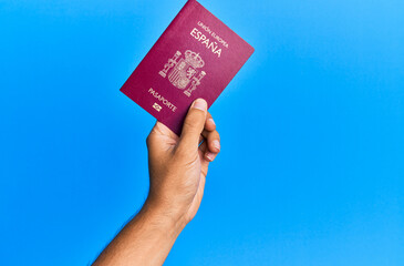 Hand of hispanic man holding spanish passport over isolated blue background.
